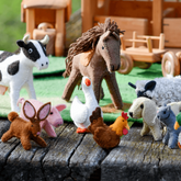 A set of handcrafted felt farm animal toys including a horse, cow, pig, sheep, rabbit, goose, dog, cat, duck, and chicken, displayed on a wooden surface.
