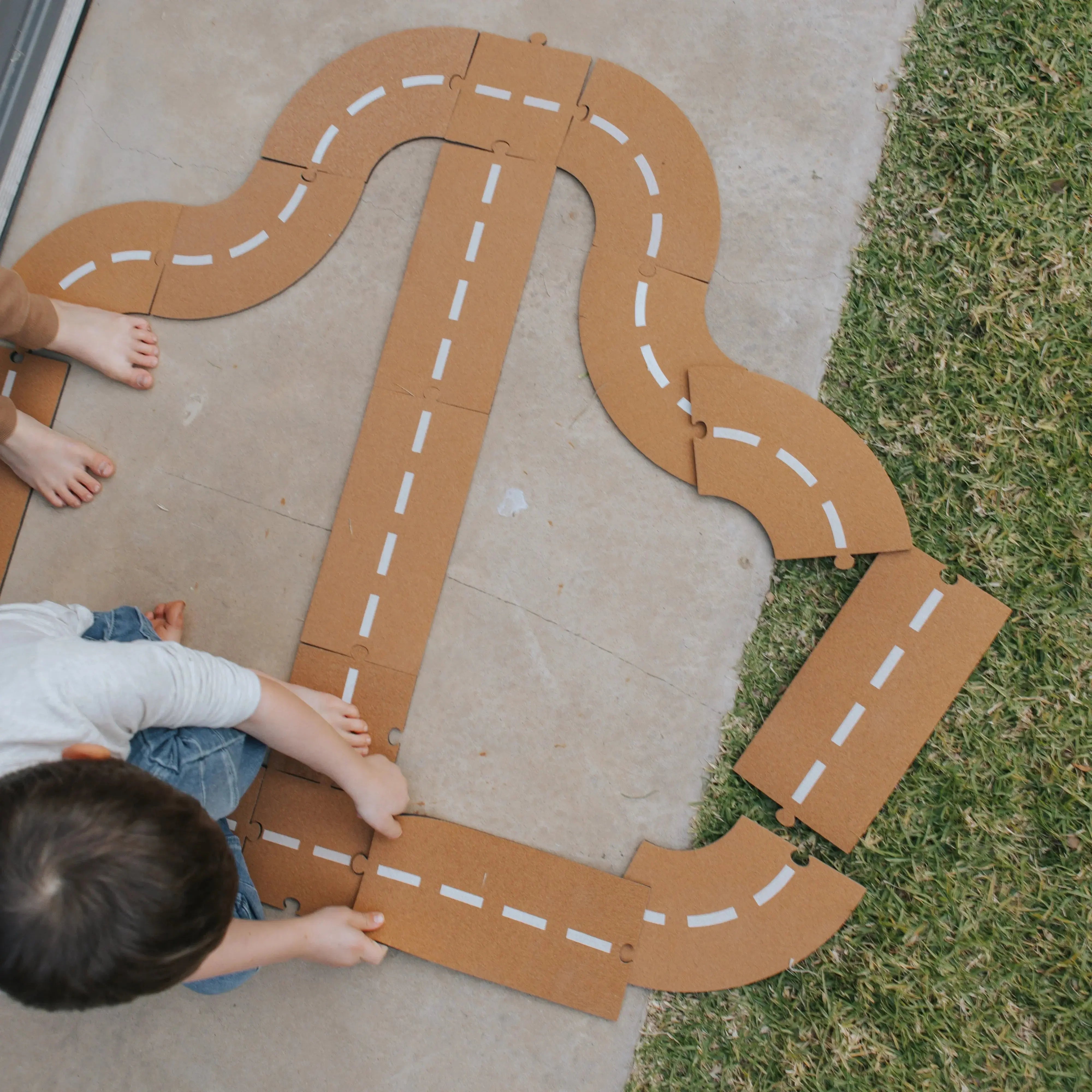 Child playing with a cork road on a driveway