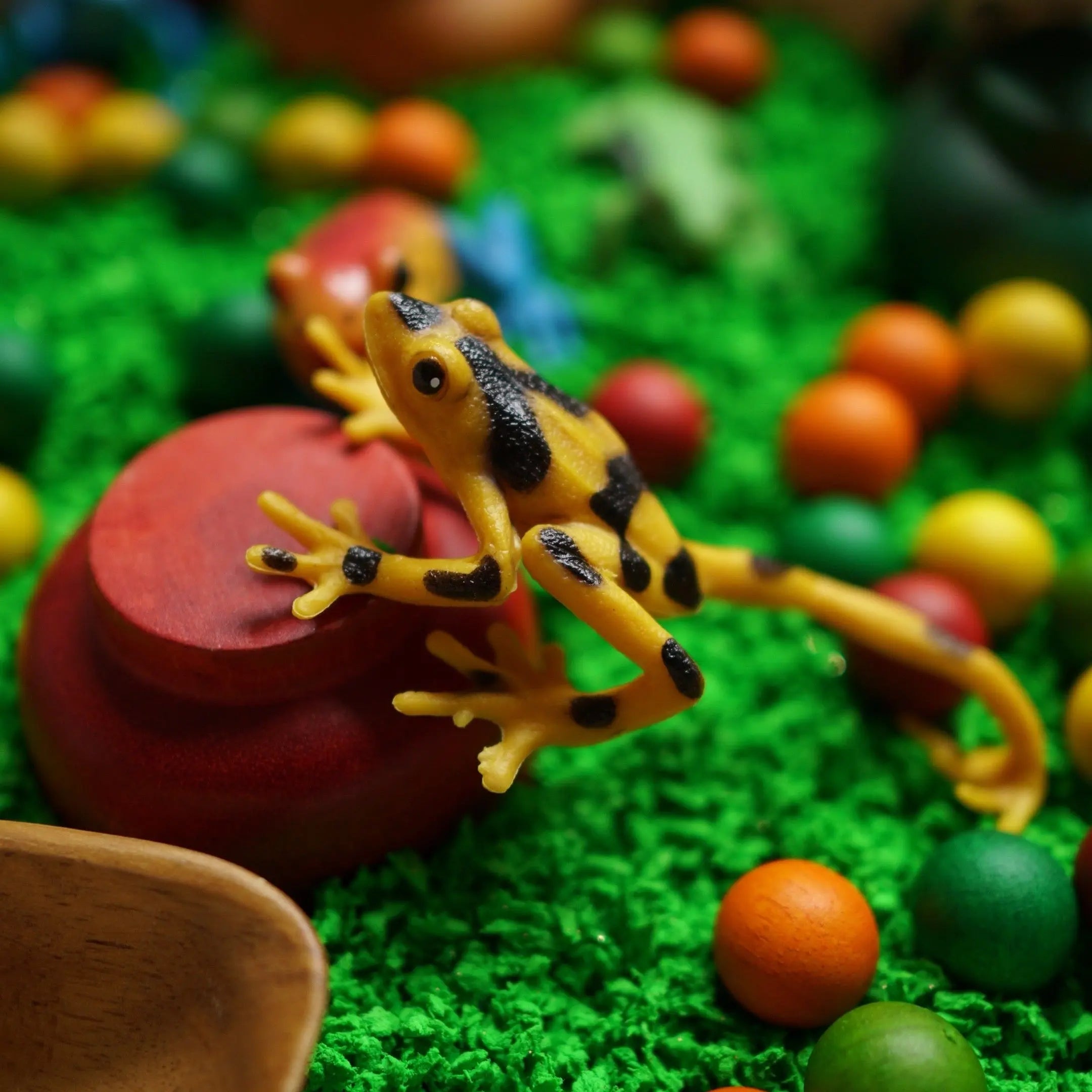 Toy frog on a red block with colorful balls and green grass-like surface
