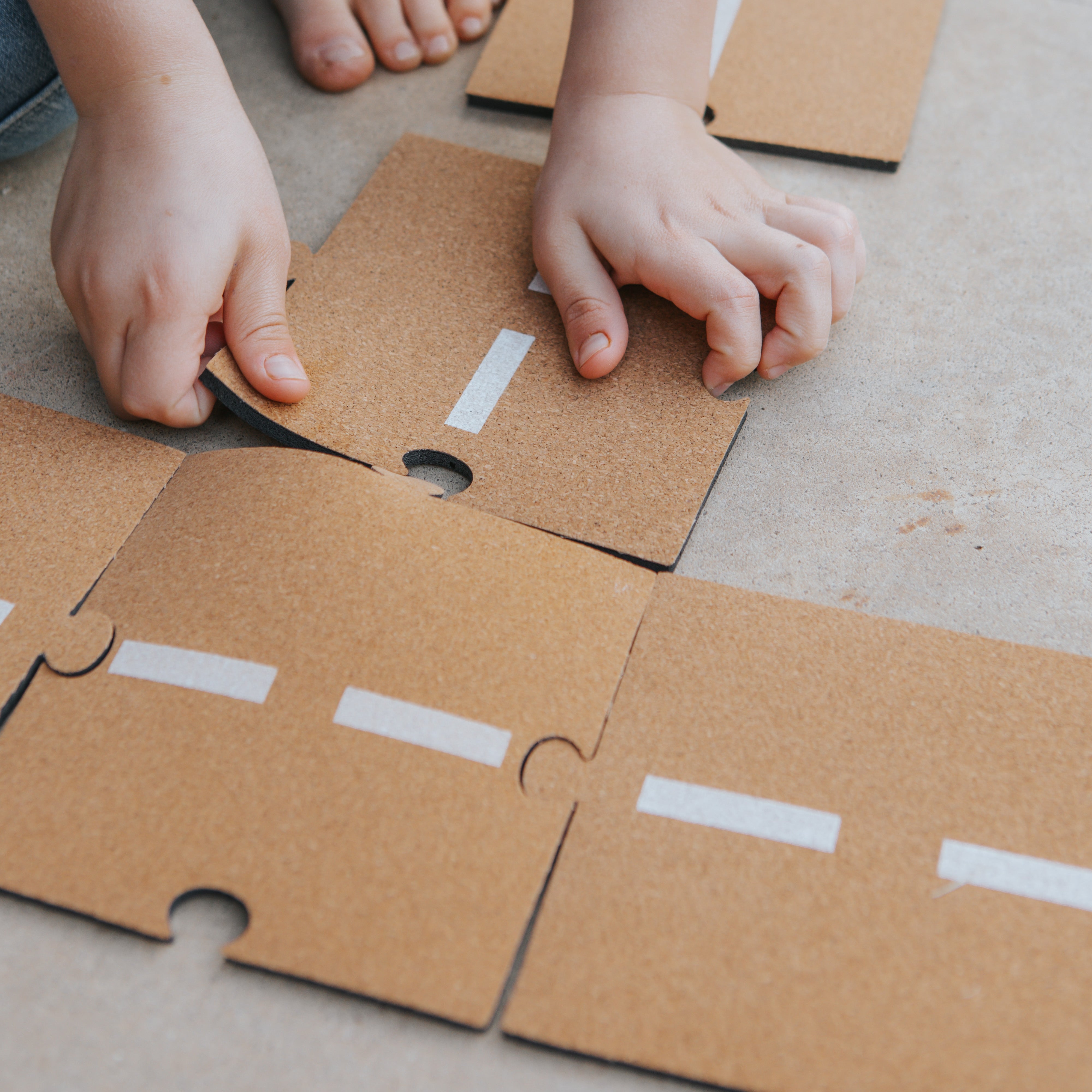 Children playing with a cork road toy on a wooden floor.

