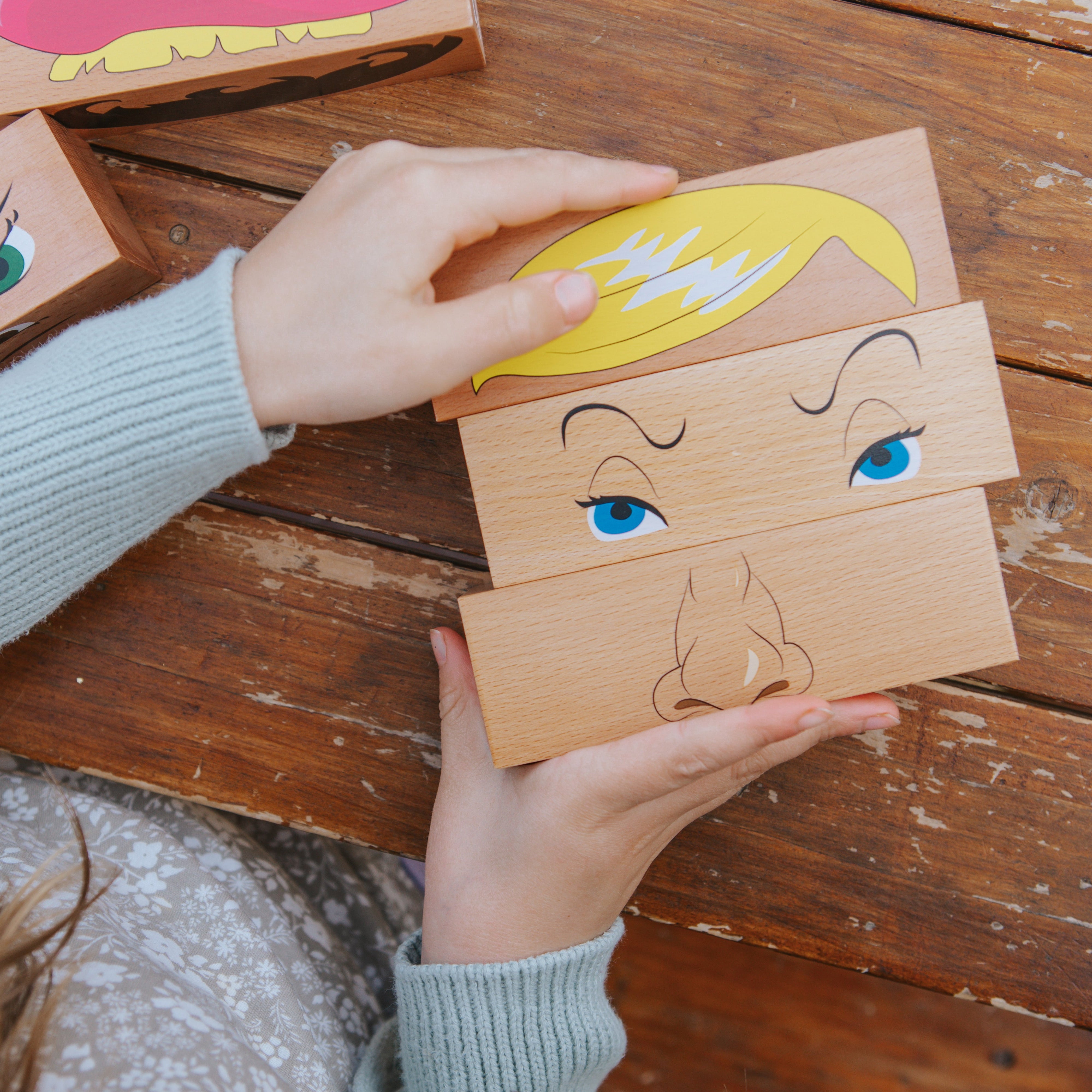 Person assembling a wooden toy with facial features on a wooden surface