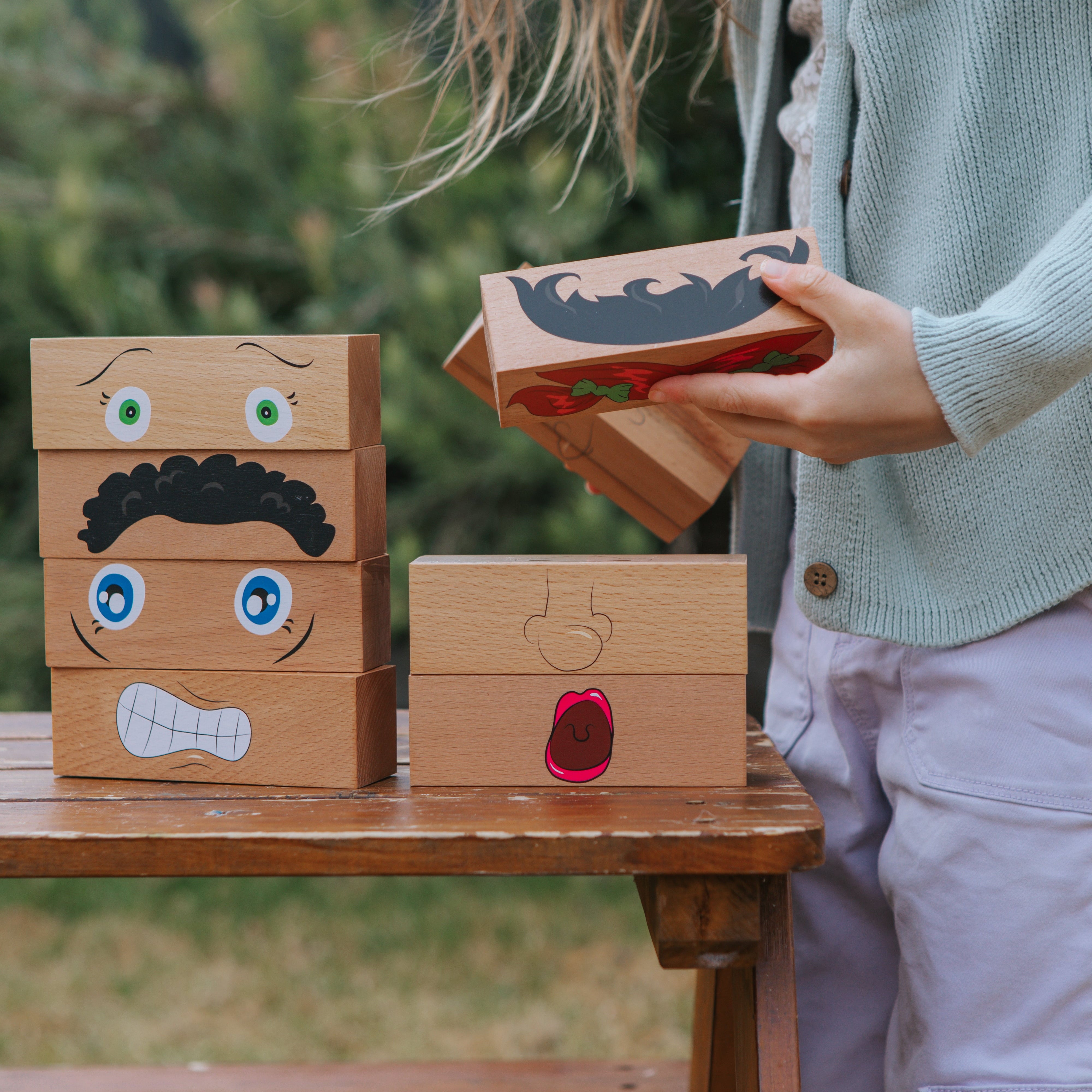 Person playing with wooden blocks shaped like faces outdoors