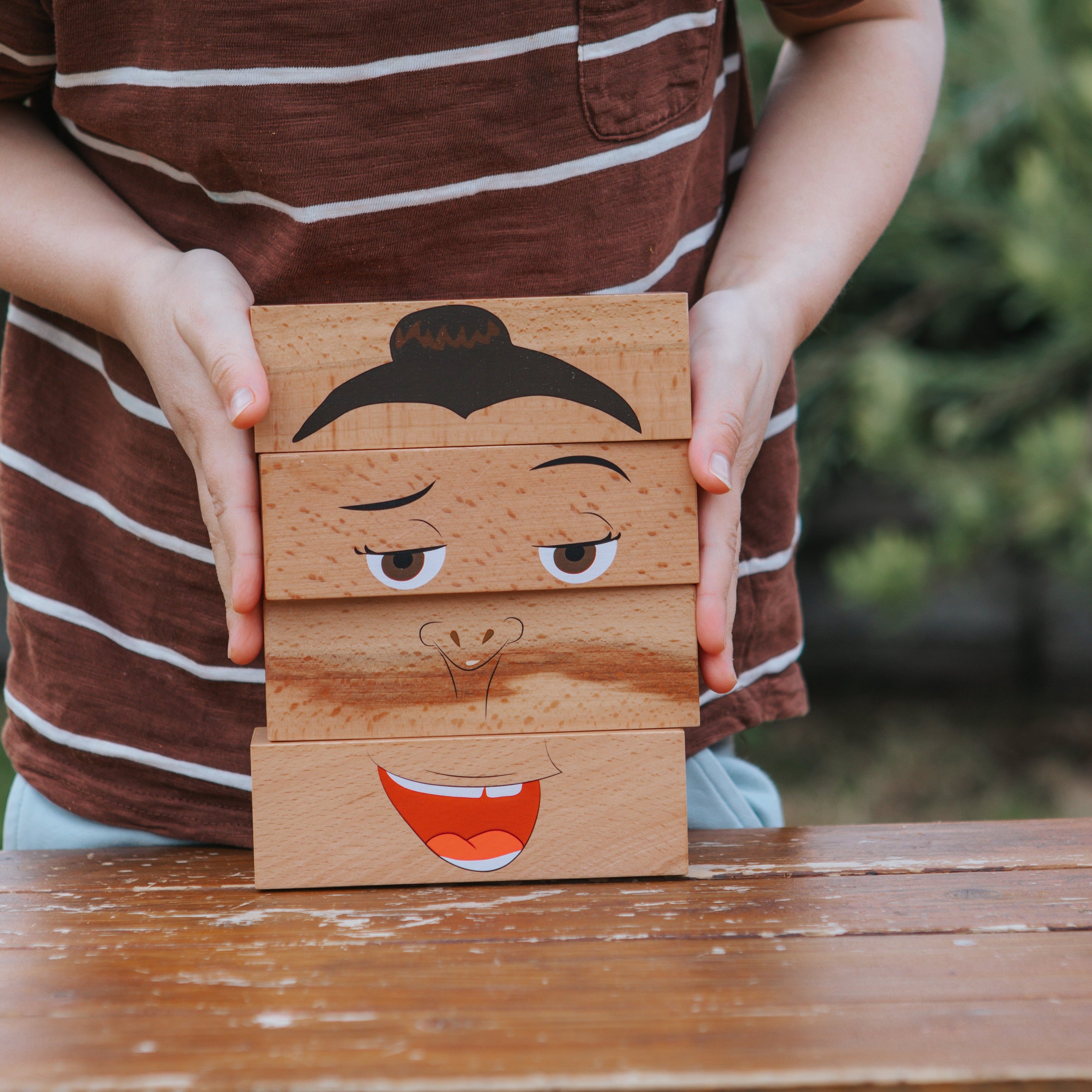 Child holding a wooden block with a face design outdoors