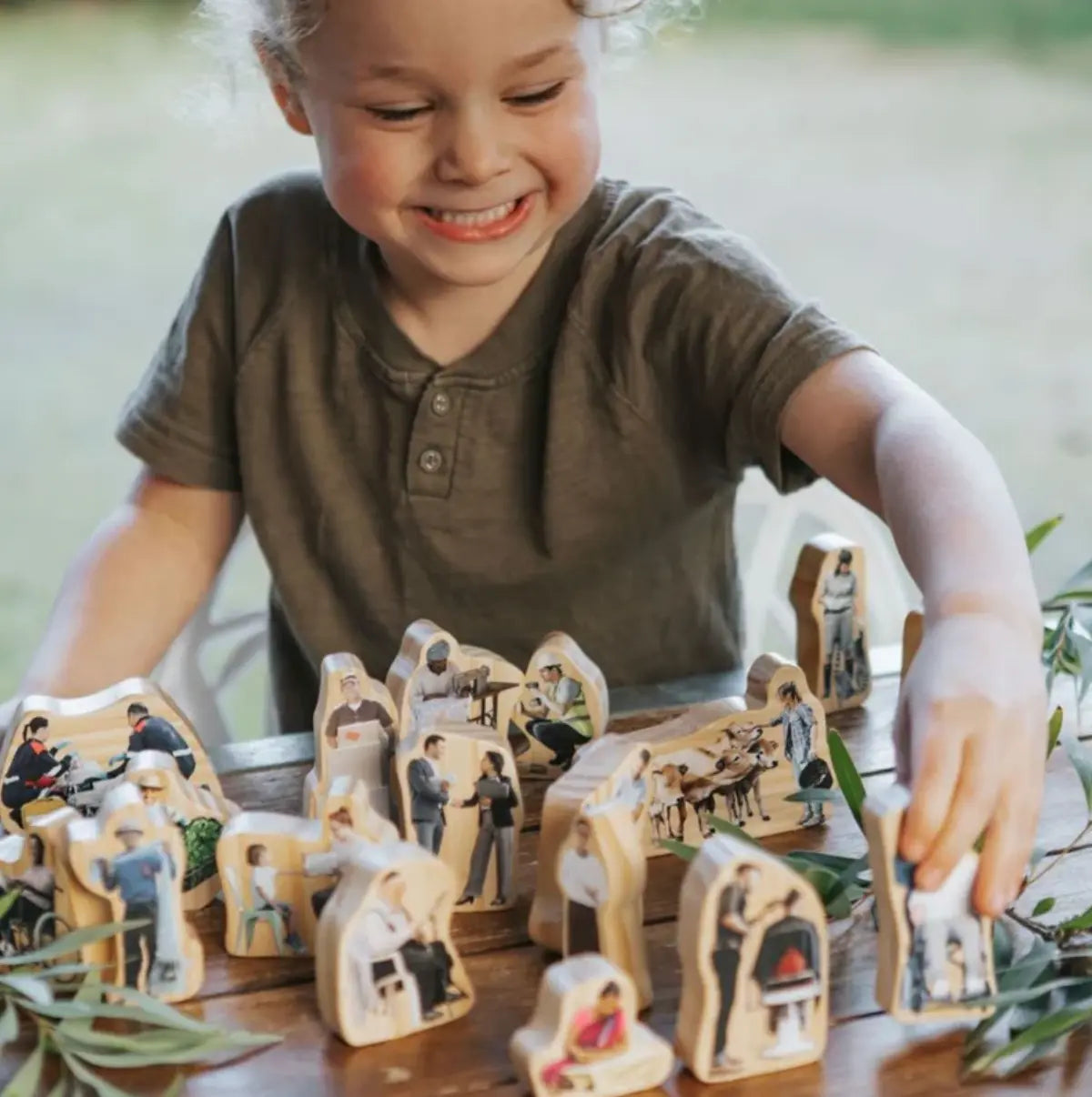 Child playing with wooden figurines on a table outdoors community role play